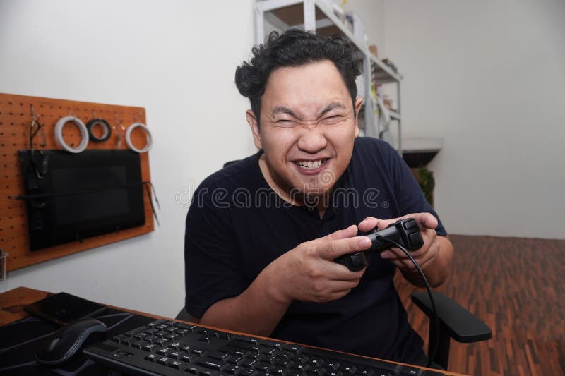 Uomo asiatico che gioca ai videogiochi con un computer felice espressione sorridente mentre regge la console immagini stock