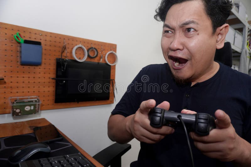 Uomo asiatico che gioca ai videogiochi con un computer felice espressione sorridente mentre regge la console fotografia stock libera da diritti