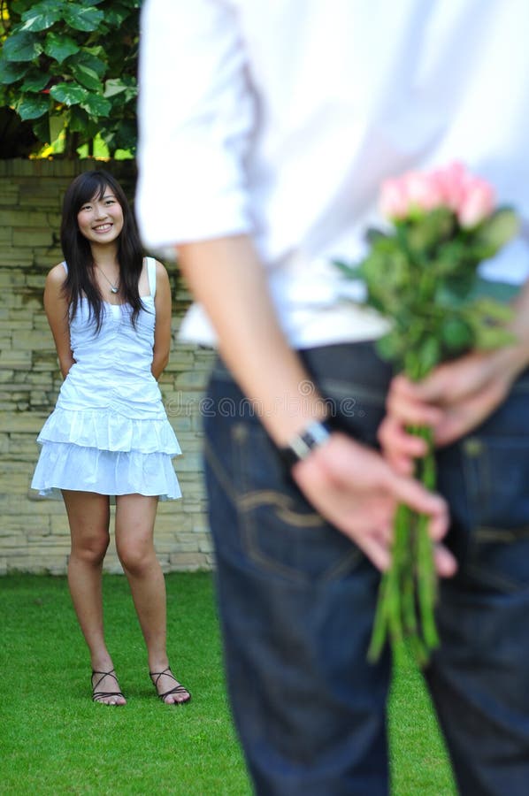 Man Holding A Bouquet Of Pink Roses With Beautiful Asian Woman Standing In The Background. Man Holding A Bouquet Of Pink Roses With Beautiful Asian Woman Standing In The Background.