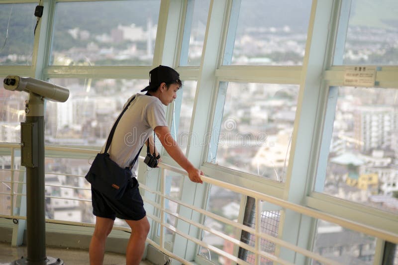 Uomo asiatico del ritratto che guarda la vista della città dall'alta torre, torre di Beppu, nel Giappone fotografia stock Uomo asiatico del ritratto che guarda la vista della città dall'alta torre, torre di Beppu, nel Giappone fotografia stock