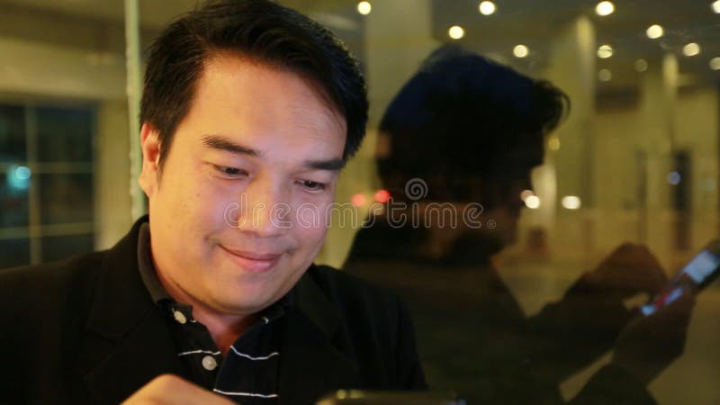 Uomo asiatico di affari che usando sul telefono cellulare ed utilizzando Smart Phone alla notte nel caffè Uomo bello che aspetta