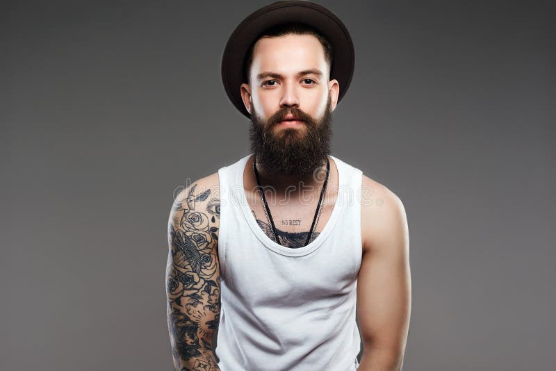 Uomo barbuto in cappello ragazzo dei pantaloni a vita bassa con il tatuaggio