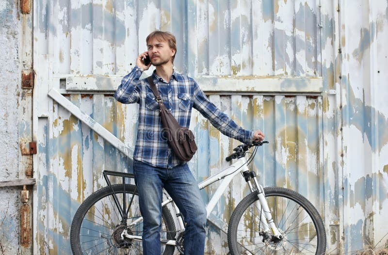 Uomo barbuto dei pantaloni a vita bassa con la bicicletta e borsa di cuoio, colloqui su astuto immagine stock libera da diritti Uomo barbuto dei pantaloni a vita bassa con la bicicletta e borsa di cuoio, colloqui su astuto immagine stock libera da diritti