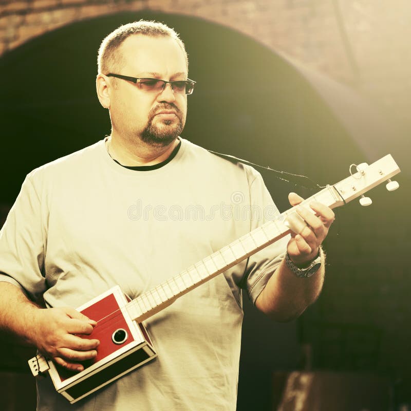 Uomo bello che gioca la sua chitarra del contenitore di sigaro immagini stock libere da diritti
