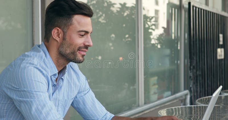 Uomo bello felice che per mezzo del suo computer portatile stock footage