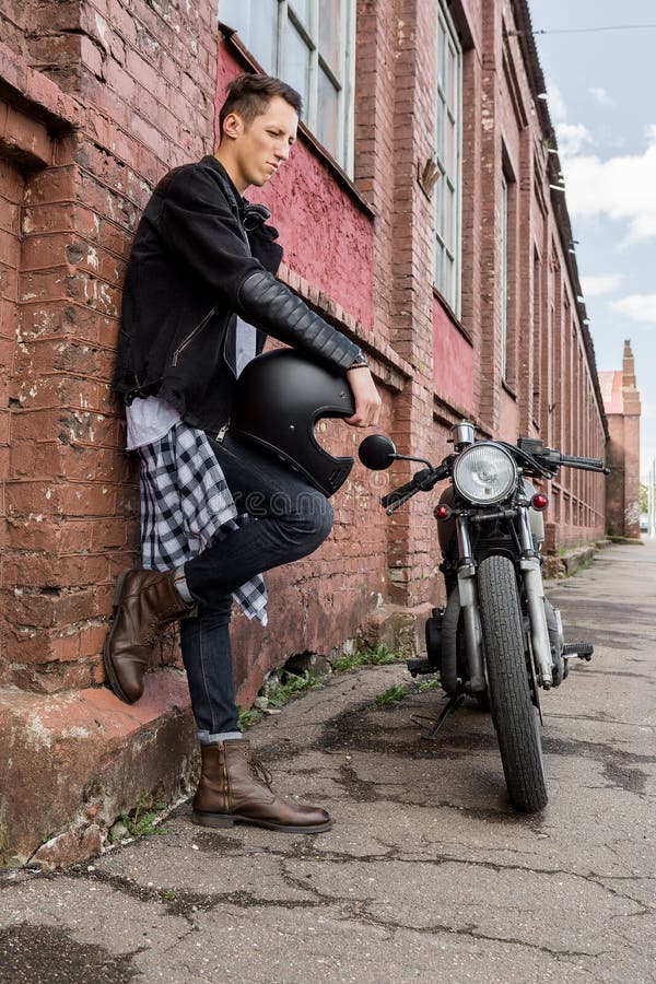 Uomo brutale vicino alla sua motocicletta di abitudine del corridore del caffè immagine stock Uomo brutale vicino alla sua motocicletta di abitudine del corridore del caffè immagine stock