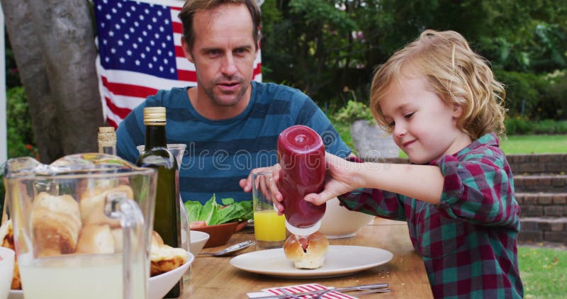 Uomo caucasico sorridente che guarda un figlio che usa il ketchup durante i festeggiamenti in giardino