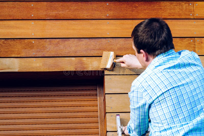 Uomo che dipinge parete di legno con una spazzola fotografie stock Uomo che dipinge parete di legno con una spazzola fotografie stock