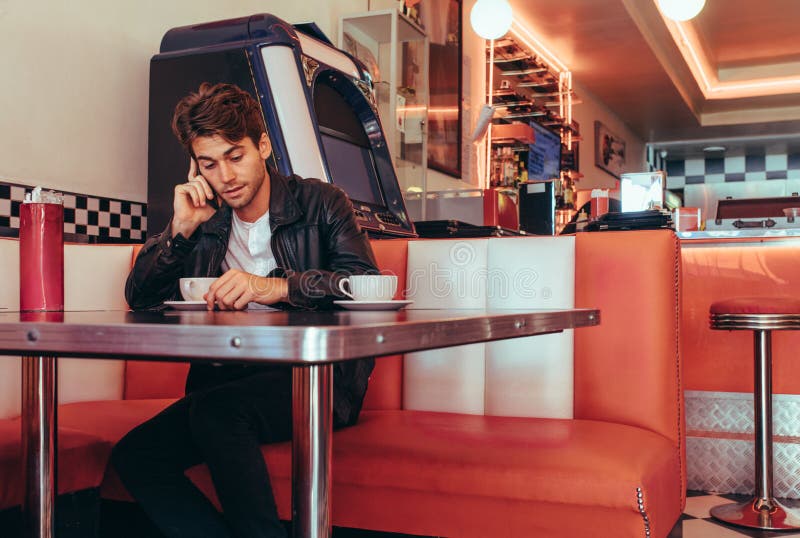 Uomo che discute a fondo telefono cellulare che si siede ad un ristorante fotografia stock Uomo che discute a fondo telefono cellulare che si siede ad un ristorante fotografia stock