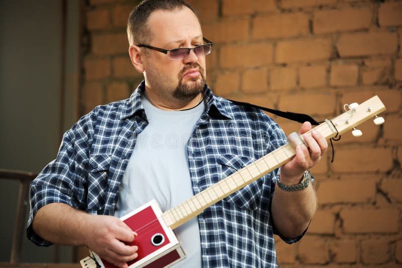 Uomo che gioca la sua chitarra del contenitore di sigaro fotografia stock