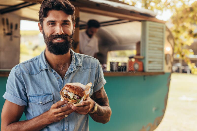 Uomo che mangia l'hamburger del camion dell'alimento fotografie stock libere da diritti Uomo che mangia l'hamburger del camion dell'alimento fotografie stock libere da diritti