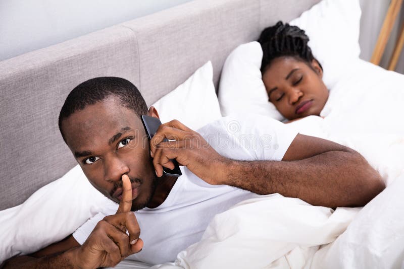 Uomo che parla segreto sul cellulare mentre il suo sonno della moglie immagine stock libera da diritti Uomo che parla segreto sul cellulare mentre il suo sonno della moglie immagine stock libera da diritti