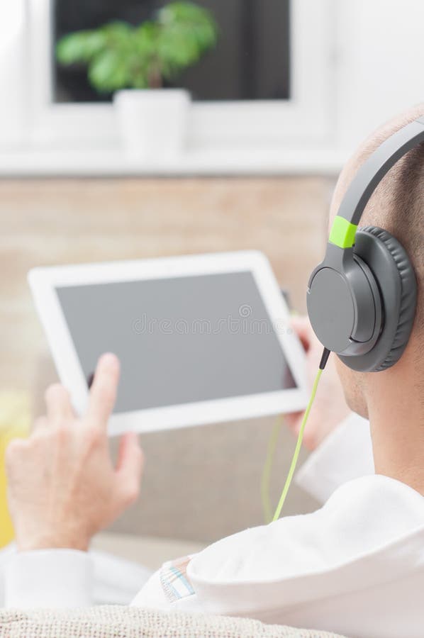 Uomo che per mezzo del computer digitale della compressa a casa che indossa le cuffie immagine stock libera da diritti Uomo che per mezzo del computer digitale della compressa a casa che indossa le cuffie immagine stock libera da diritti
