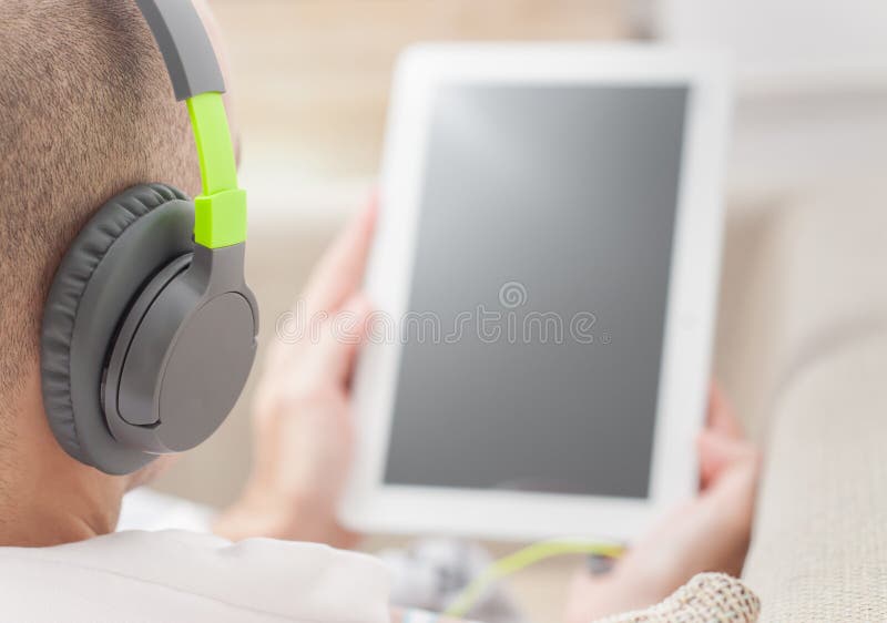 Uomo che per mezzo del computer digitale della compressa a casa che indossa le cuffie fotografia stock libera da diritti Uomo che per mezzo del computer digitale della compressa a casa che indossa le cuffie fotografia stock libera da diritti