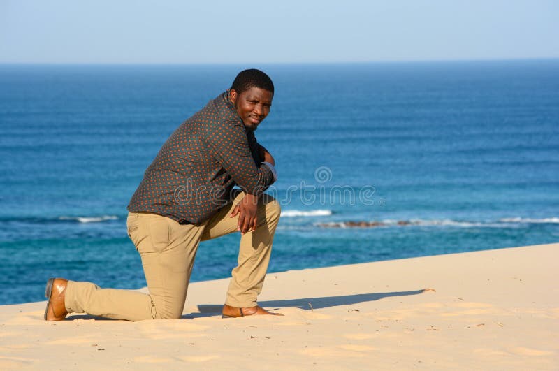 Uomo che si inginocchia sulla spiaggia fotografie stock Uomo che si inginocchia sulla spiaggia fotografie stock