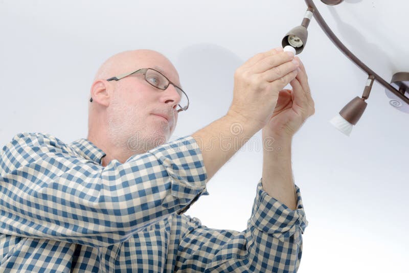 Uomo che sostituisce la lampadina a casa fotografia stock libera da diritti Uomo che sostituisce la lampadina a casa fotografia stock libera da diritti