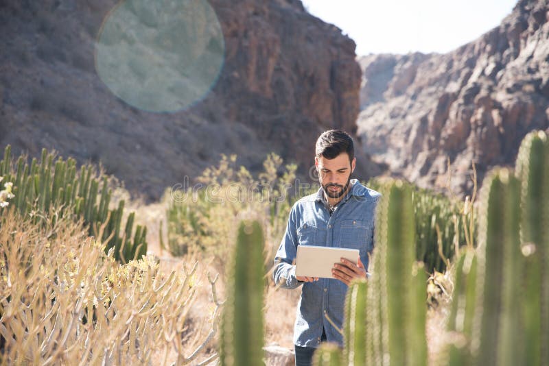 Uomo che sta accanto ad un cactus che guarda giù fotografia stock libera da diritti Uomo che sta accanto ad un cactus che guarda giù fotografia stock libera da diritti