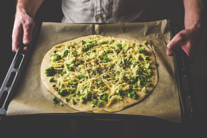Uomo che tiene pizza cruda con i broccoli ed il formaggio fotografia stock Uomo che tiene pizza cruda con i broccoli ed il formaggio fotografia stock