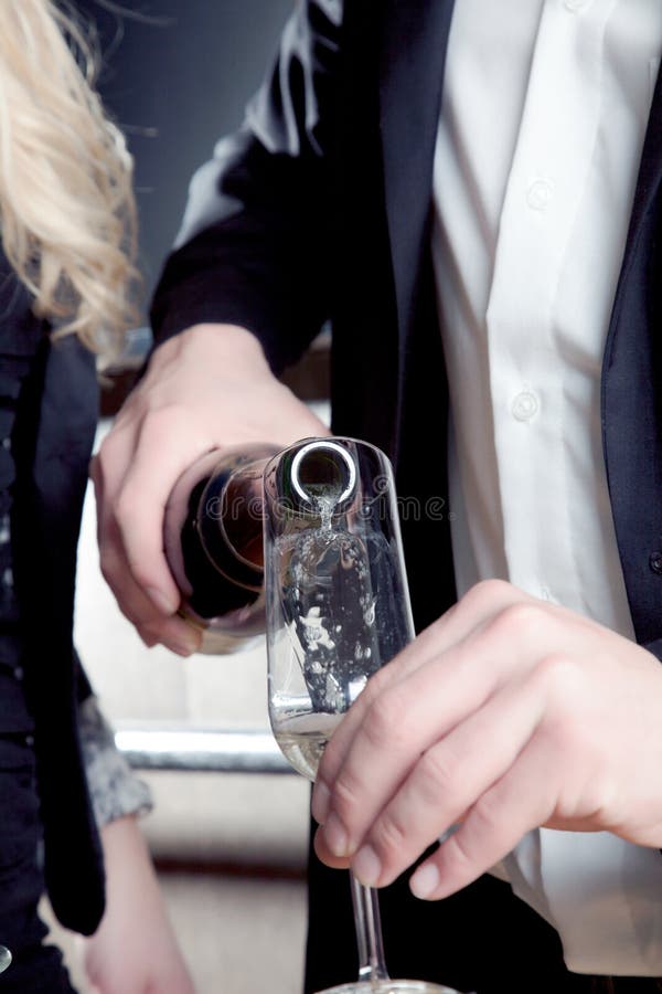 Man pouring sparkling bubbly champagne into an elegant flute or glass in preparation for sharing a special toast with his female partner, cropped view of the hands. Man pouring sparkling bubbly champagne into an elegant flute or glass in preparation for sharing a special toast with his female partner, cropped view of the hands