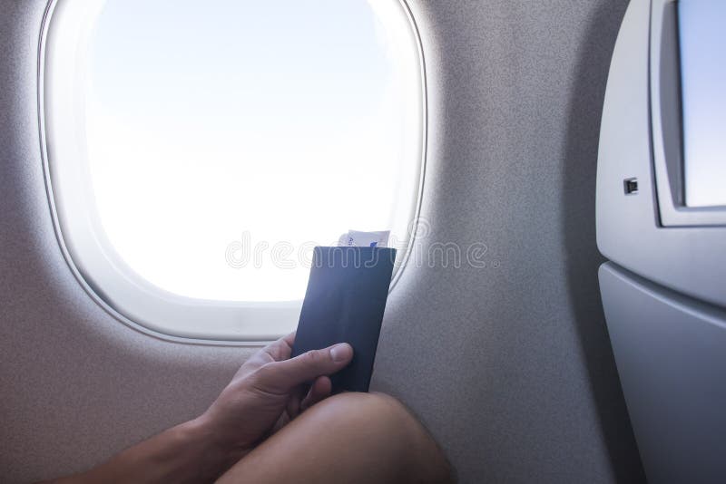 Uomo con il passaporto e biglietto che si siede accanto alla finestra nel viaggio di vacanza dell'aeroplano della cabina di aerei
