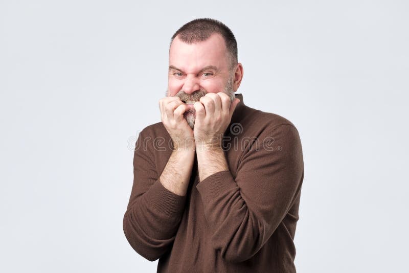Uomo con la barba nelle unghie mordenti della camicia marrone nel timore fotografia stock Uomo con la barba nelle unghie mordenti della camicia marrone nel timore fotografia stock