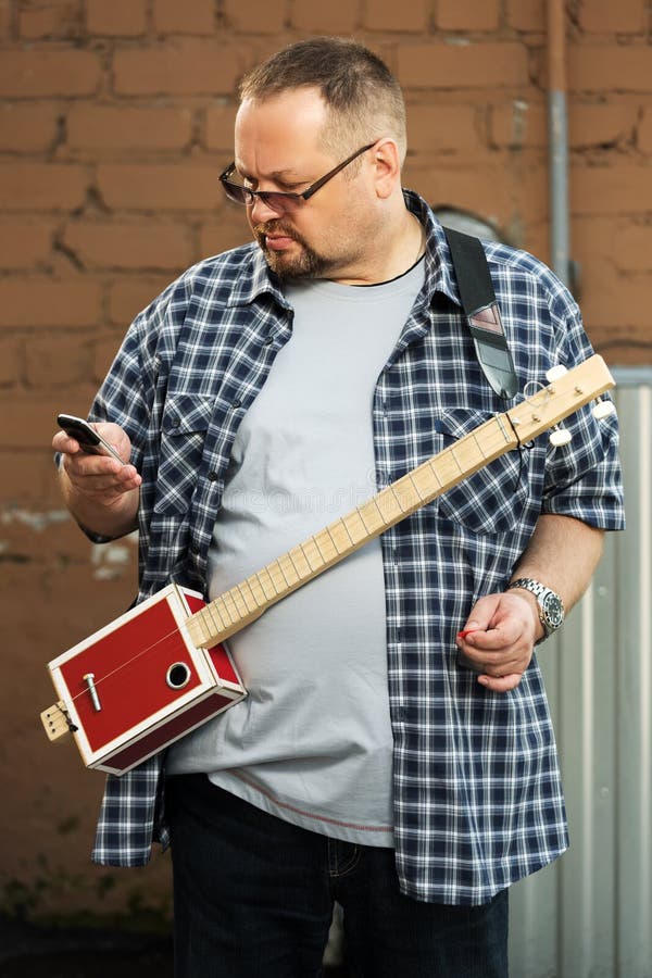 Uomo con una chitarra del contenitore di sigaro che esamina telefono cellulare immagini stock libere da diritti