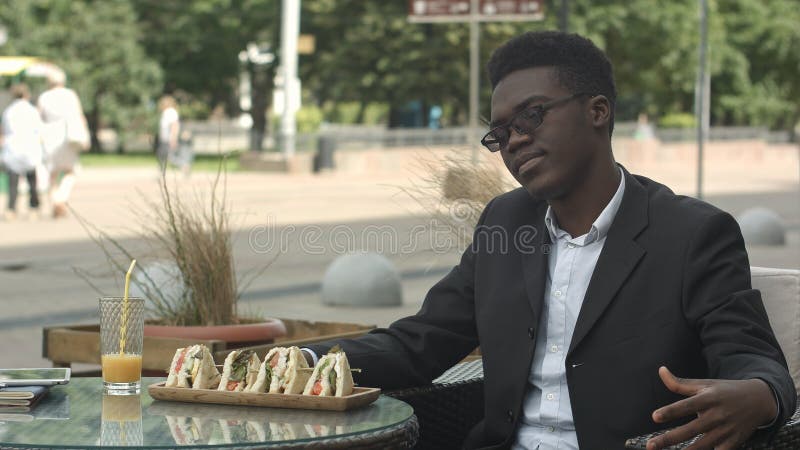 Uomo d'affari afroamericano stanco che si siede in caffè che sembra annoiato o alimentato su fotografia stock Uomo d'affari afroamericano stanco che si siede in caffè che sembra annoiato o alimentato su fotografia stock