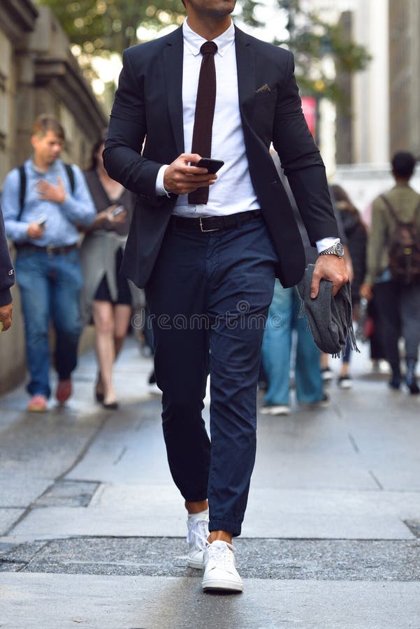 Uomo d'affari alla moda alla moda che cammina sulla via della città e che manda un sms sul telefono cellulare fotografie stock