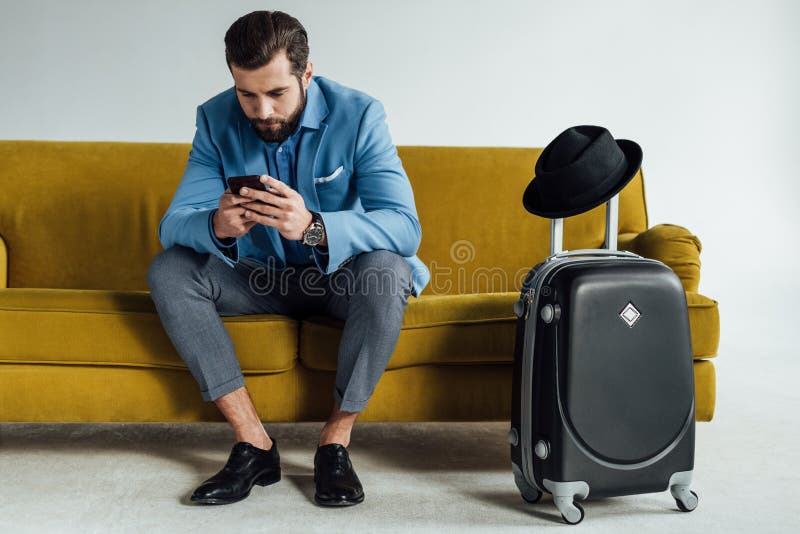 uomo d'affari alla moda bello facendo uso dello smartphone e sedersi sul sofà fotografia stock uomo d'affari alla moda bello facendo uso dello smartphone e sedersi sul sofà fotografia stock