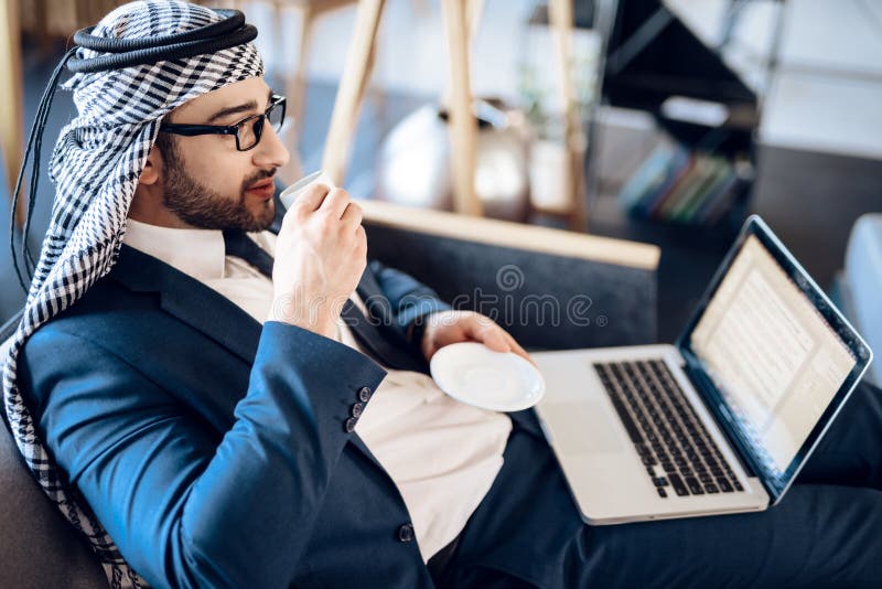 Uomo d'affari arabo rilassato su lapton con caffè sullo strato a camera di albergo fotografie stock libere da diritti Uomo d'affari arabo rilassato su lapton con caffè sullo strato a camera di albergo fotografie stock libere da diritti