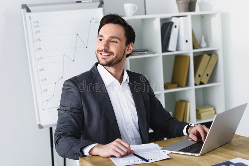 uomo d'affari bello sorridente che si siede alla tavola ed a distogliere lo sguardo fotografia stock uomo d'affari bello sorridente che si siede alla tavola ed a distogliere lo sguardo fotografia stock