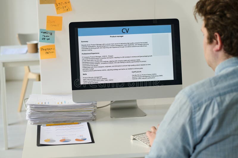 Rear view of young businessman sitting at his workplace and using computer to post his resume online. Rear view of young businessman sitting at his workplace and using computer to post his resume online