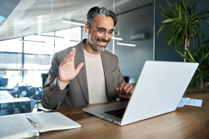 Uomo d'affari di mezza età felice che lavora in modo ibrido per riunioni virtuali in ufficio. fotografie stock