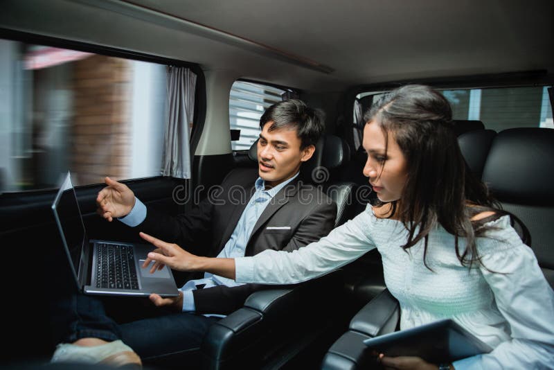 Uomo d'affari e donna che per mezzo del computer portatile sul sedile del passeggero dell'automobile fotografia stock Uomo d'affari e donna che per mezzo del computer portatile sul sedile del passeggero dell'automobile fotografia stock