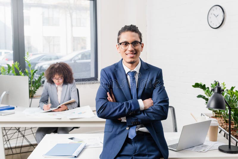 Uomo d'affari sorridente che sta nell'ufficio con il suo collega femminile dalla tavola fotografie stock Uomo d'affari sorridente che sta nell'ufficio con il suo collega femminile dalla tavola fotografie stock