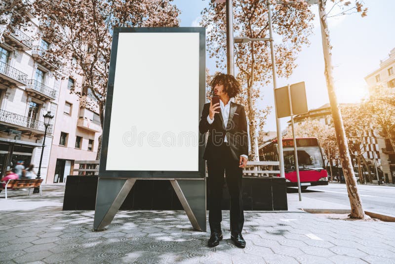Uomo d'affari in vestito convenzionale vicino al modello urbano vuoto dell'insegna fotografia stock Uomo d'affari in vestito convenzionale vicino al modello urbano vuoto dell'insegna fotografia stock
