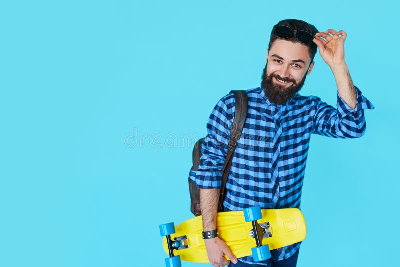 Uomo dei pantaloni a vita bassa sopra fondo blu variopinto che tiene pattino giallo fotografia stock libera da diritti Uomo dei pantaloni a vita bassa sopra fondo blu variopinto che tiene pattino giallo fotografia stock libera da diritti