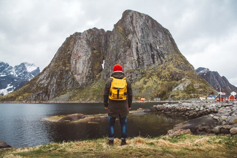 Uomo del viaggiatore con uno zaino giallo che indossa una condizione rossa del cappello sui precedenti della montagna e del lago immagini stock libere da diritti Uomo del viaggiatore con uno zaino giallo che indossa una condizione rossa del cappello sui precedenti della montagna e del lago immagini stock libere da diritti