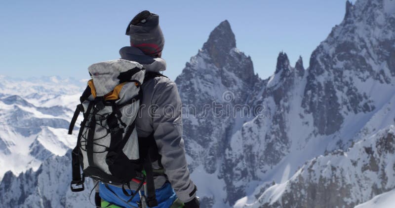 Uomo dell'alpinista dello scalatore che raggiunge la cima nevosa del supporto con la piccozza da ghiaccio nel giorno soleggiato A