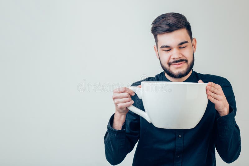 Uomo di affari che tiene una tazza enorme e surdimensionata divertente di caffè nero in caffeina