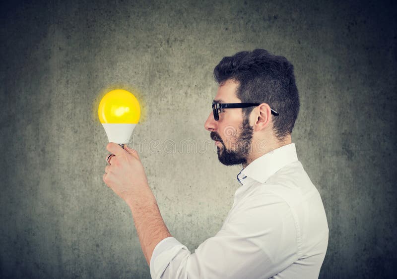 Uomo di affari con l'espressione premurosa che esamina la lampadina della luce intensa fotografie stock libere da diritti Uomo di affari con l'espressione premurosa che esamina la lampadina della luce intensa fotografie stock libere da diritti