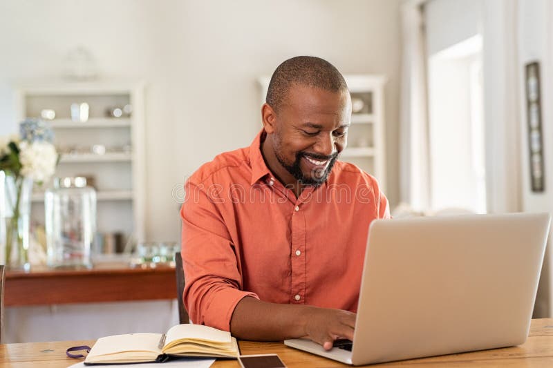 Uomo di colore maturo felice che per mezzo del computer portatile immagini stock libere da diritti