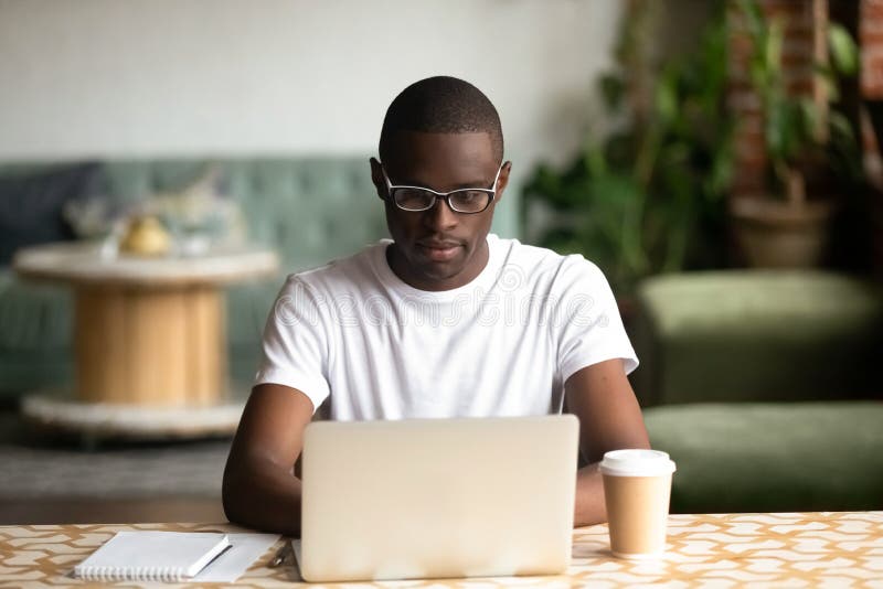 Uomo di colore messo a fuoco che studia sul caffè bevente del computer portatile immagine stock libera da diritti