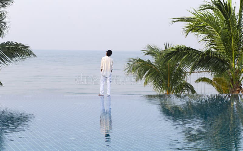Uomo di stile di vita ai margini della piscina, che guarda mare e cielo fotografia stock libera da diritti