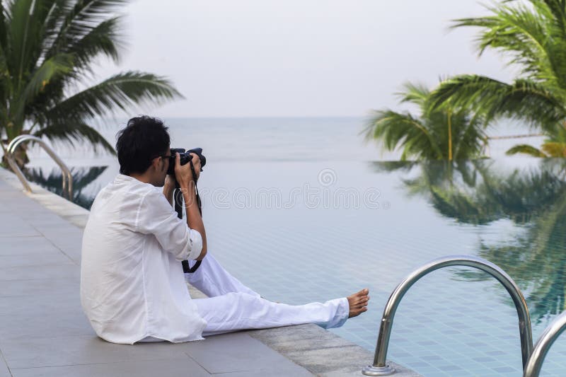 Uomo di strada seduto a fare una foto in piscina in località turistica immagini stock libere da diritti