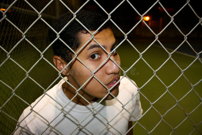 A young hispanic male looking through fence. A young hispanic male looking through fence.