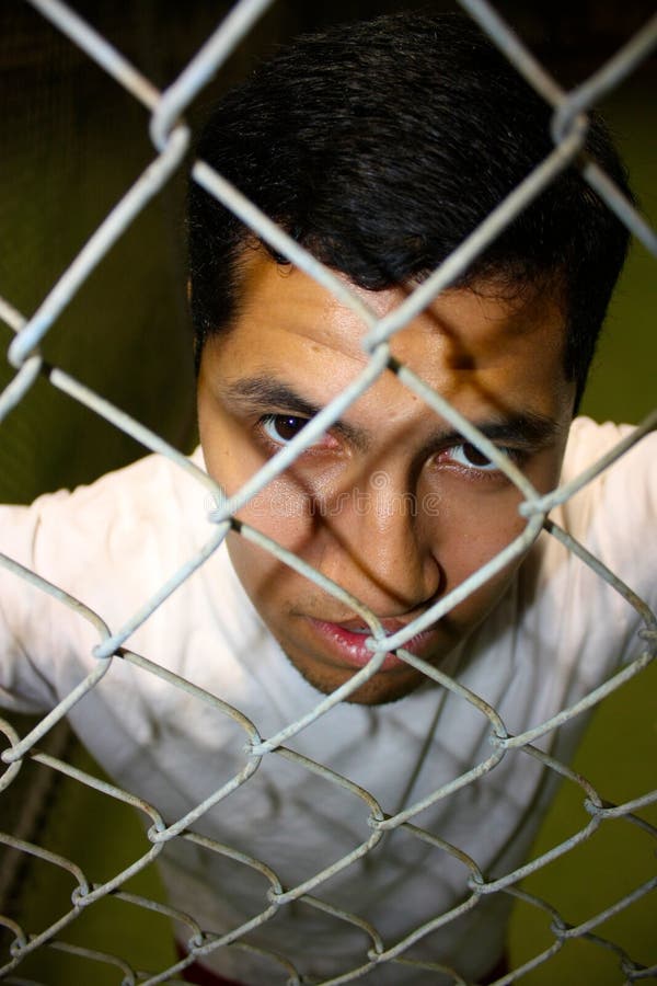 A young hispanic male looking through fence. A young hispanic male looking through fence.