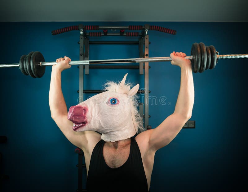 Funny man in comical mask doing sport exercise. Unusual guy pump up iron at home. Unicorn sportsman. Funny man in comical mask doing sport exercise. Unusual guy pump up iron at home. Unicorn sportsman.