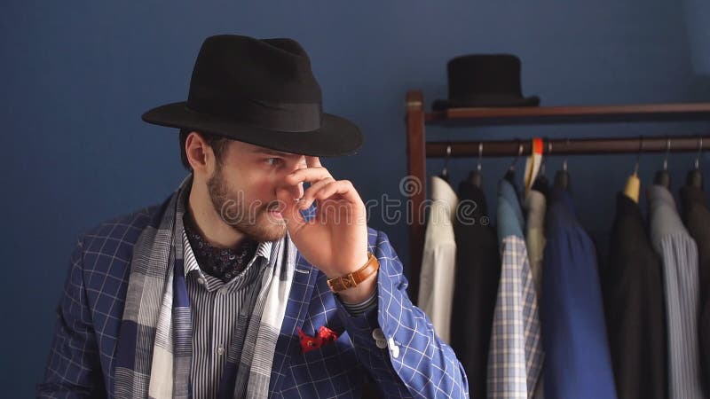 Uomo elegante nel vestito di modo e cappello che posa all'atelier con la bevanda