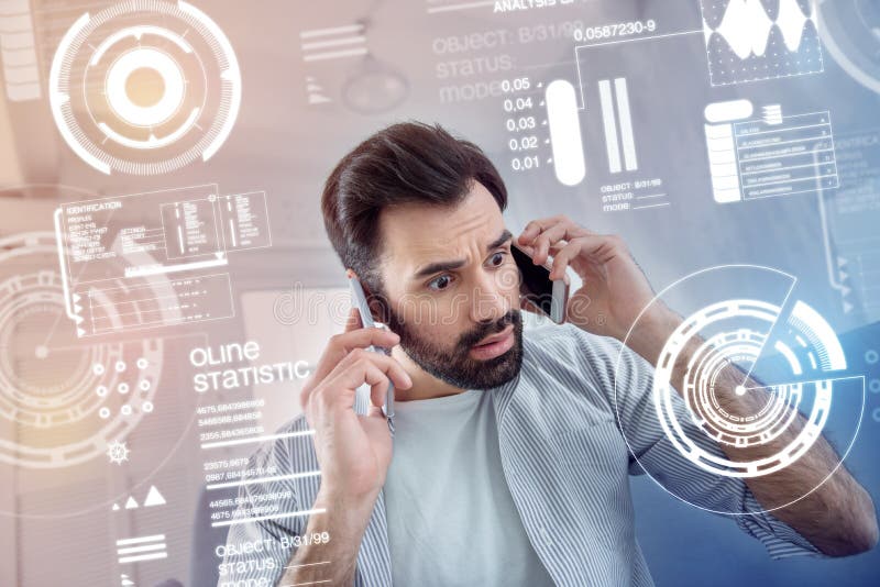 Uomo emozionale che preme due telefoni alla sua formica delle orecchie che sembra preoccupata immagine stock libera da diritti Uomo emozionale che preme due telefoni alla sua formica delle orecchie che sembra preoccupata immagine stock libera da diritti